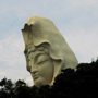 Der Kopf einer riesigen Kanon-Statue schaut aus einem Wald heraus